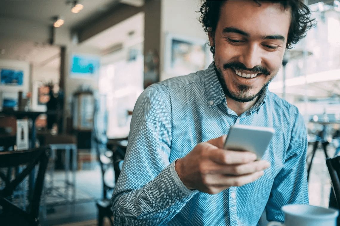 A man is smiling while looking at his cell phone.