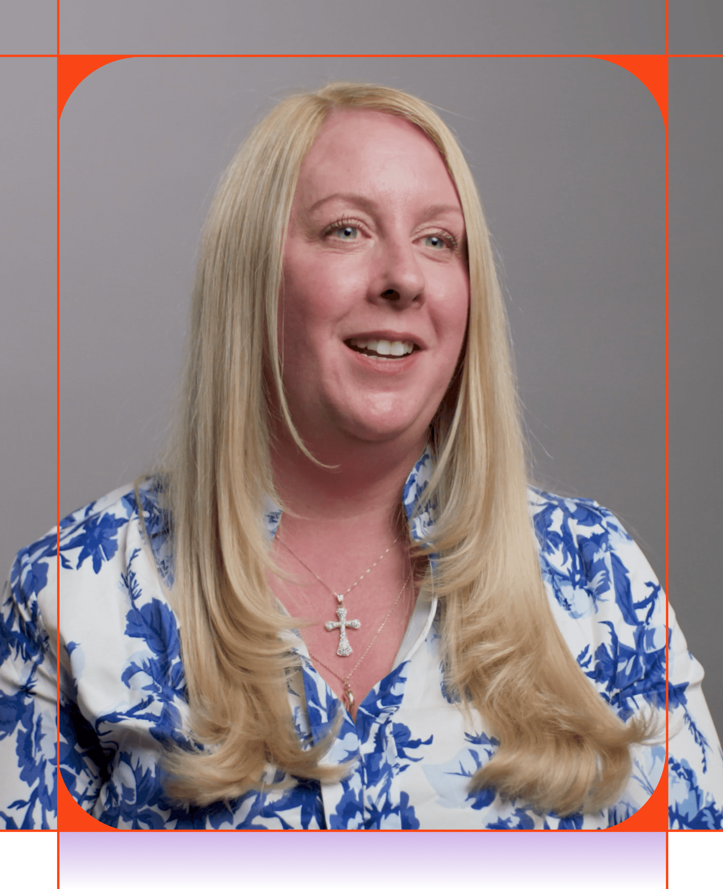 Eine lächelnde Frau mit langen blonden Haaren trägt ein weiß-blaues Blumenhemd und eine Kreuzkette.
